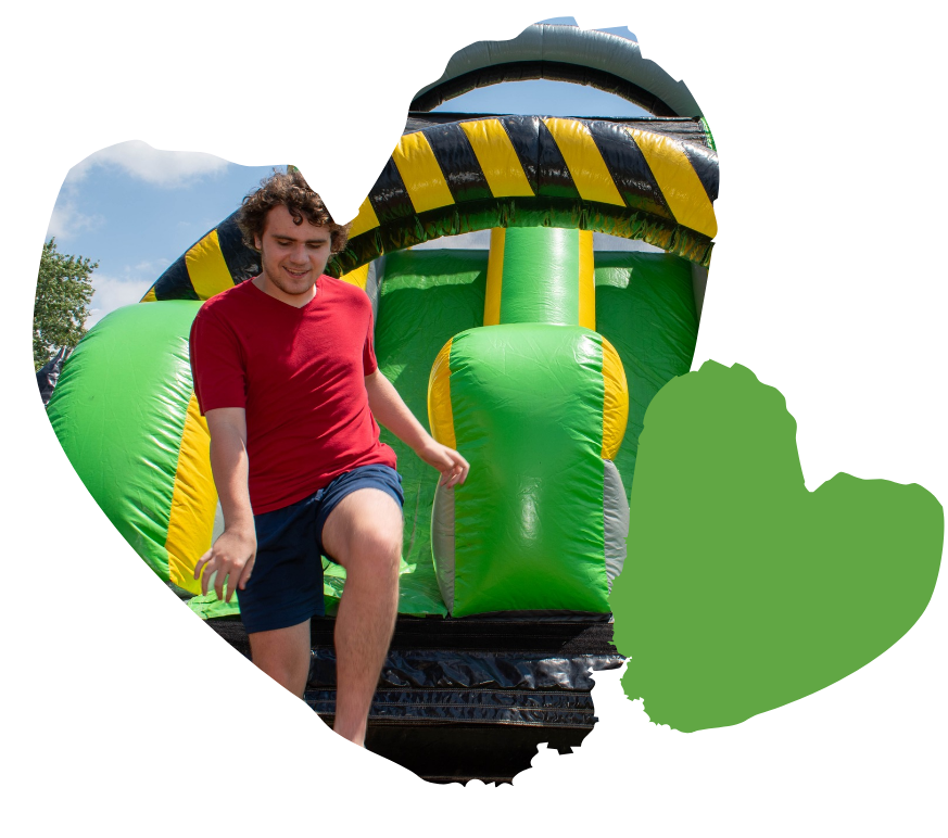 A person in a red shirt exits a colorful inflatable obstacle course, smiling under the sunny sky.