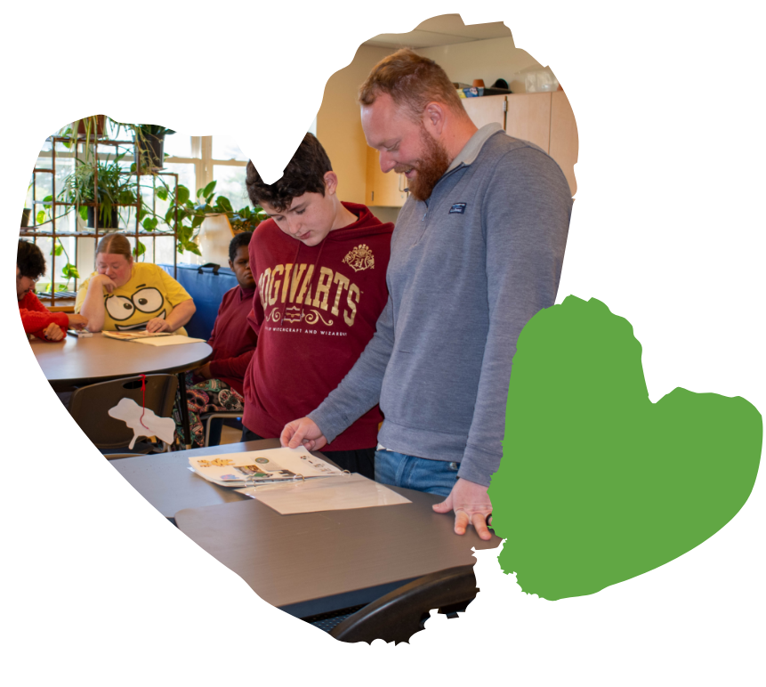 student and adult flipping though book on desk in classroom