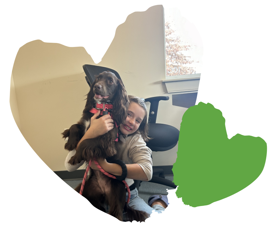In an office setting, a child gleefully hugs a brown dog, embodying the warmth and support often found in behavioral services.