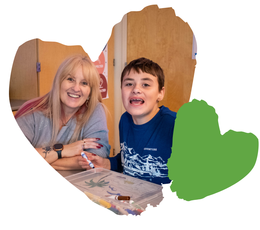 Woman and boy smiling while doing arts and crafts at a table.