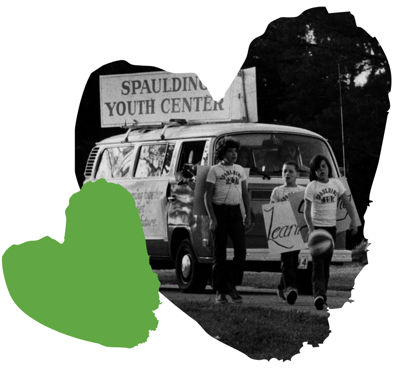 Three people walking in parade with a Spaulding Youth Center sign, carrying a ball.