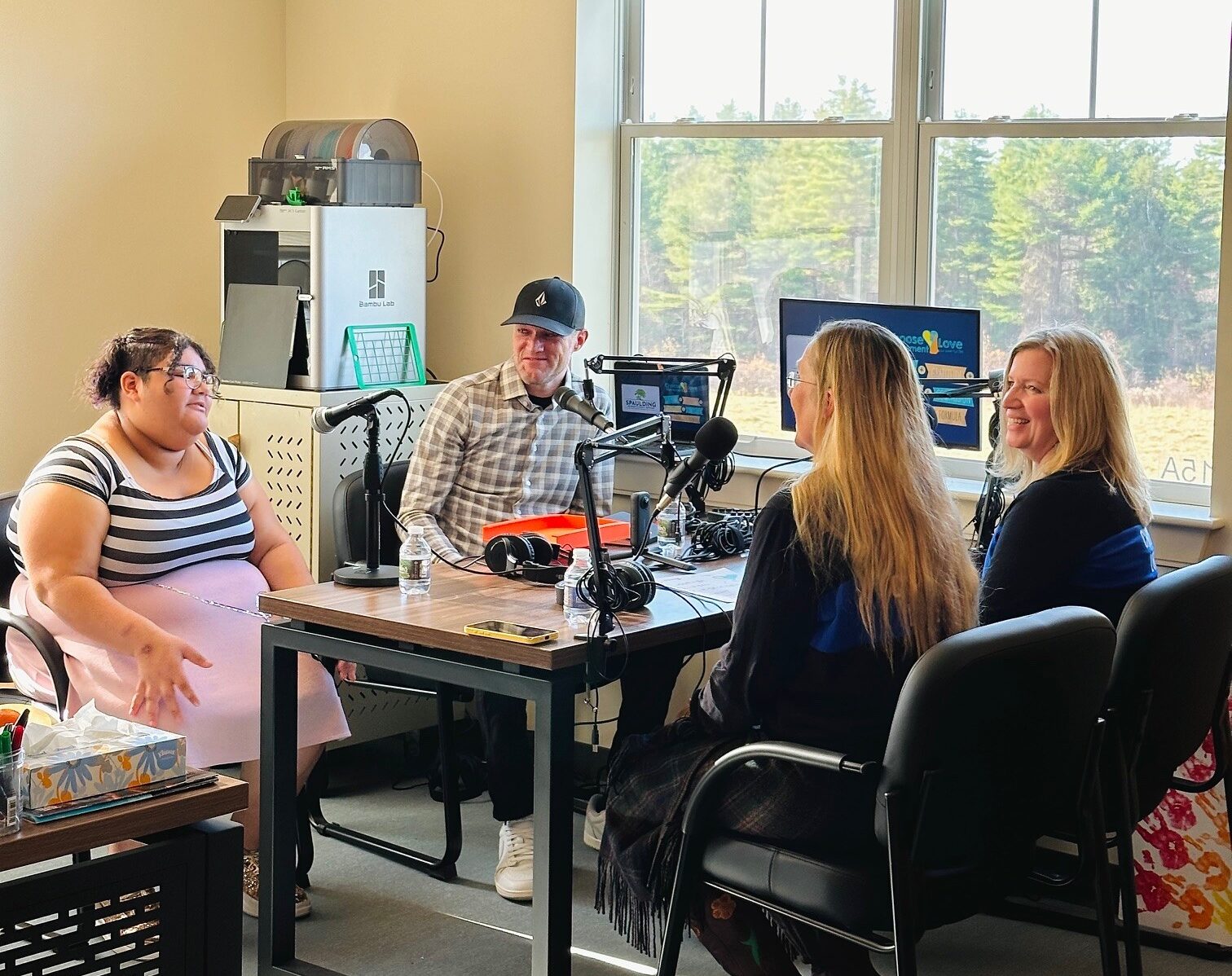 Four people having a discussion in a podcast recording studio with microphones and equipment on the table.