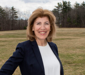 Rebecca MacLennan in a blazer standing outdoors in a grassy field with trees in the background.