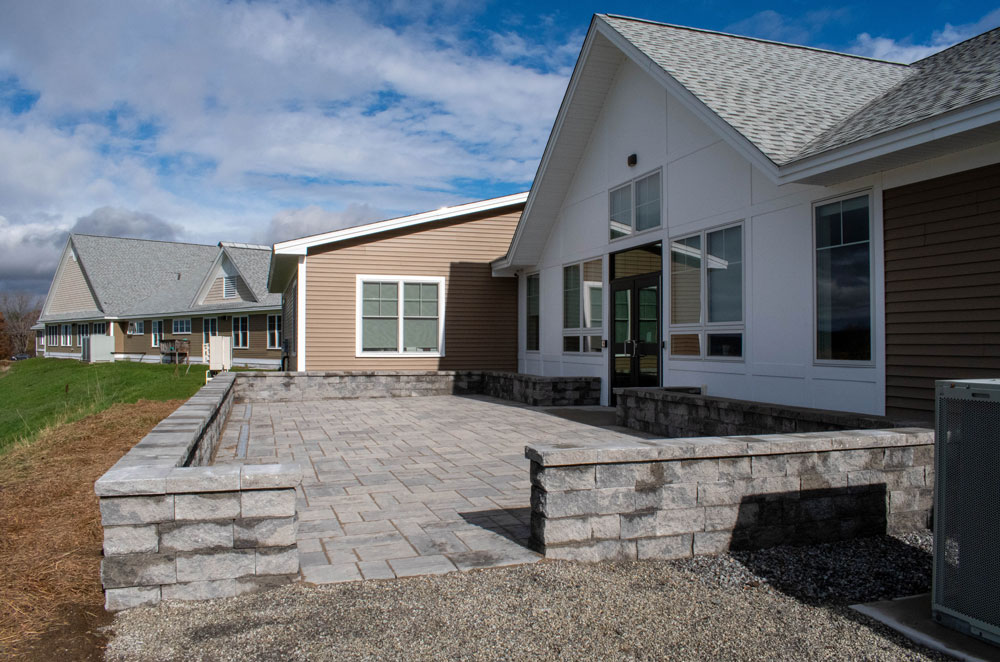 Single-story houses with gray roofs and stone patios under a partly cloudy sky.