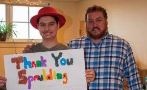 Two people smiling, one holding a colorful thank you poster with Star Wars drawings and messages.