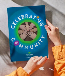 Hands hold a blue brochure titled Celebrating Community with a photo of joined hands in the center.