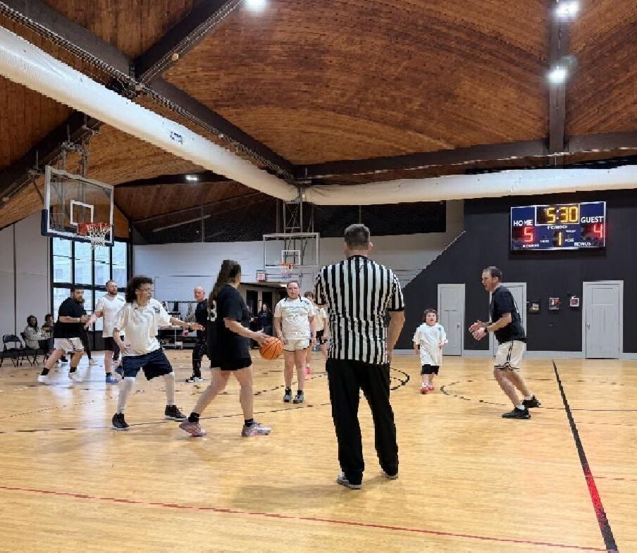People play basketball in a gym with a referee watching; the scoreboard shows 5-4 with 5:30 left.