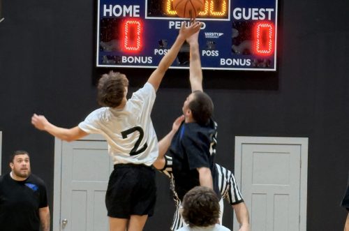 Two youth basketball players jump for the ball at tip-off, while a referee and others watch the action.