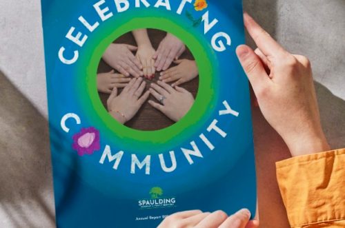 Hands hold a blue brochure titled Celebrating Community with a photo of joined hands in the center.