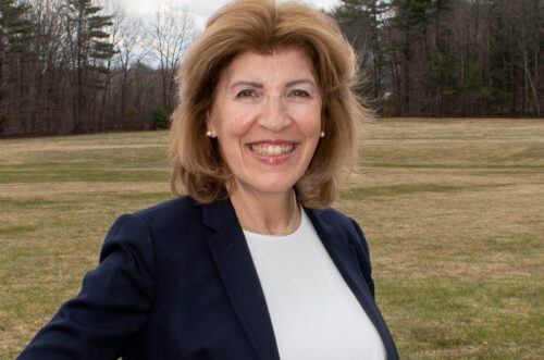 Smiling woman in a blazer standing outdoors in a grassy field with trees in the background. Rebecca MacLennan in a blazer standing outdoors in a grassy field with trees in the background.