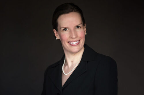Smiling person in a black suit and pearl necklace against a dark background. Smiling person in a black suit and pearl necklace against a dark background.