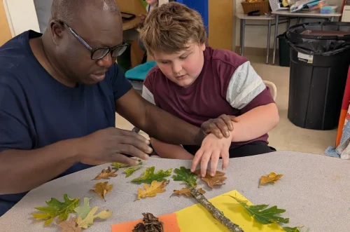 A teacher and student sorting autumn leaves on a table.