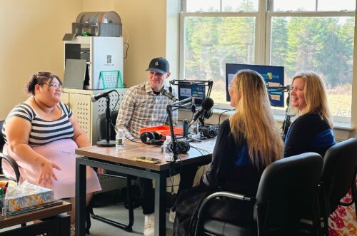 Four people having a discussion in a podcast recording studio with microphones and equipment on the table. Four people having a discussion in a podcast recording studio with microphones and equipment on the table.